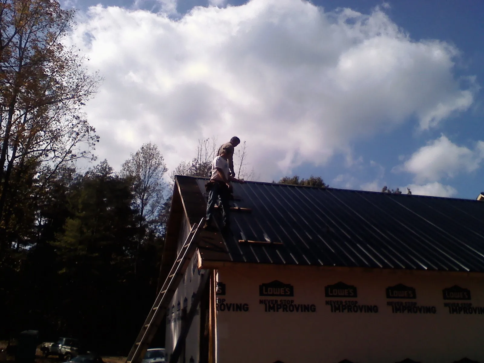 Roofer fastening dark metal panels high against a cloudy sky, from a Roof Inspection job in Davis